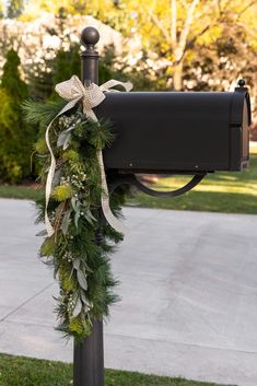 a mailbox decorated with greenery and ribbon tied around the post in front of a driveway