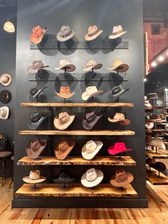 hats on display in a store with wooden flooring and black wall behind them,