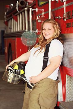 a pregnant woman standing in front of a firetruck holding a helmet and smiling