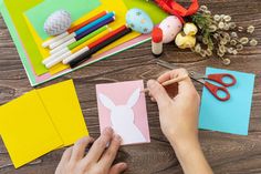 a person cutting out paper with scissors on top of a wooden table next to craft supplies