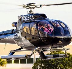 a helicopter that is flying in the air with people inside it and some trees behind it