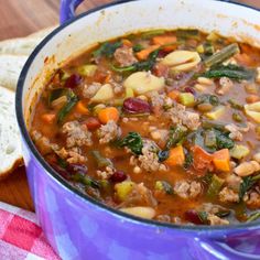 a blue pot filled with meat and vegetable soup next to bread on a checkered table cloth