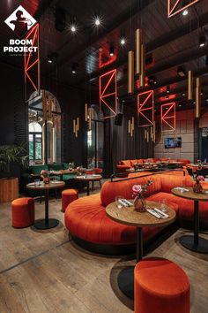 a restaurant with orange couches and round tables in the center, surrounded by hanging lights