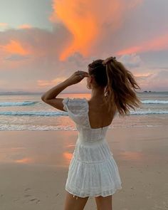 a woman is standing on the beach looking at the ocean with her hair blowing in the wind