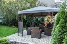 a gazebo with chairs and tables in the middle of a brick patio surrounded by greenery