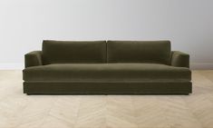 a green couch sitting on top of a hard wood floor next to a white wall