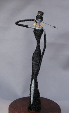 a wire sculpture of a woman holding a wand on top of a wooden stand with a white background