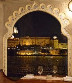 a view of a building from across the water at night with two wine glasses in front of it