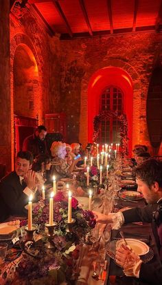 a group of people sitting around a dinner table with candles in the middle of it