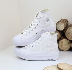 a pair of white high top sneakers sitting next to stacked wood logs on a white surface