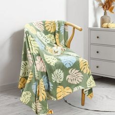 a chair with a blanket on it next to a white dresser and vase filled with flowers