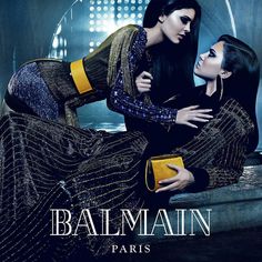 two women are sitting on a bench in front of a building with the words balmain paris