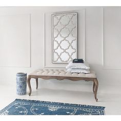 a white bench sitting in front of a mirror on top of a wooden table next to a blue vase