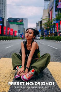 a woman sitting on the ground in front of a city street with buildings and signs