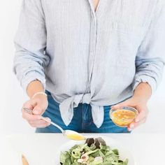 a woman is holding a spoon over a bowl of salad with dressing on the side