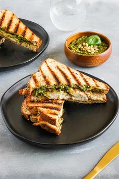 grilled sandwich with pesto and pine nuts on black plate next to bowl of pesto