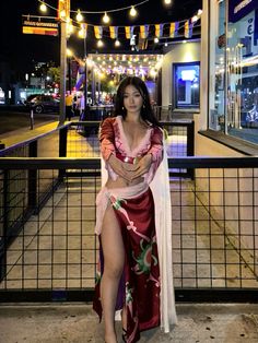 a woman in a long dress is standing on the sidewalk at night with lights strung above her