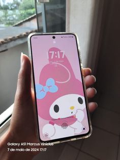 someone holding up an iphone with hello kitty on the screen in front of a window