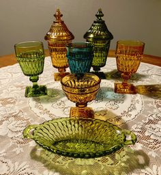 a table topped with green glass dishes and glasses on top of a white table cloth