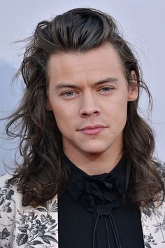 a man with long hair and flowers in front of him is looking at the camera