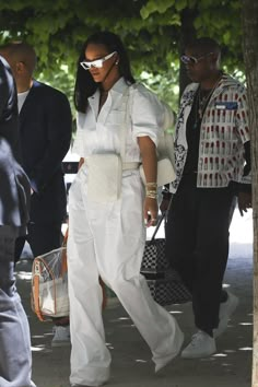 a woman wearing white is walking down the street with her handbag in her other hand