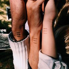 two people with matching tattoos on their arms holding each other's hands and looking at the camera