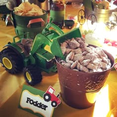 a table topped with a bucket full of food next to a toy tractor and other toys