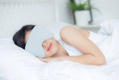 a woman laying in bed with a blindfold on her head and sleeping mask over her eyes