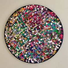 a circular artwork made out of many different colored buttons on a white wall with a black frame