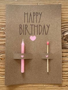 a birthday card with two matches and a pink candle on the top, sitting on a piece of brown paper