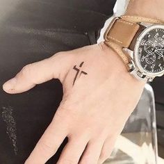 a person's hand with a wrist tattoo and a cross on the ring finger