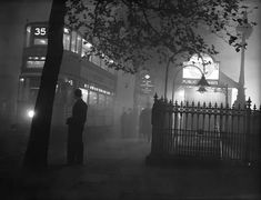 an old photo of a man standing in front of a building on a foggy night