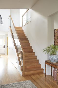 there is a wooden stair case in the living room with potted plants on the table