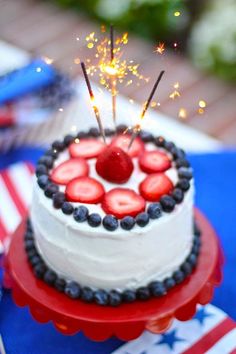 a white cake with strawberries and blueberries on top is topped with sparklers