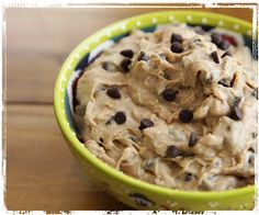 a green bowl filled with cookie dough and chocolate chips on top of a wooden table