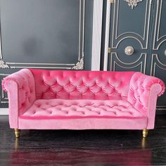 a pink couch sitting on top of a hard wood floor next to a gray wall