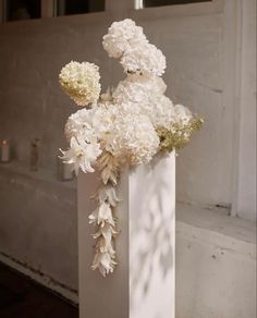 a white vase with flowers in it sitting on the ground next to a window sill