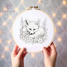 a person holding up a embroidery hoop with a drawing of a fox and flowers on it