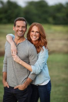 a man and woman hugging each other while standing in front of a green field with trees