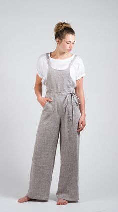 a woman standing in front of a white background wearing grey linen overalls and a white t - shirt