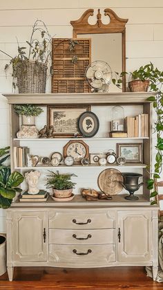 an old dresser is decorated with plants and clocks