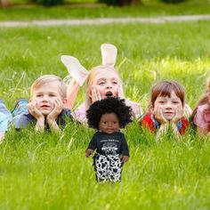 four children laying in the grass with their faces covered by fake hair and bunny ears