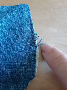 someone is stitching the edge of a pair of jeans with blue thread on a wooden surface