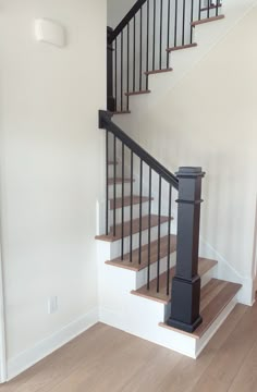 an empty room with a stair case and hard wood flooring on the bottom level