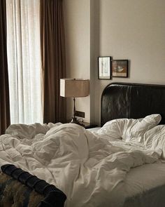 an unmade bed with white sheets and pillows in a bedroom next to a window