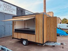 a small food truck parked in front of a building with wood panels on the side