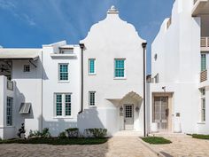 a white building with green shutters on the front and side doors is seen in this image