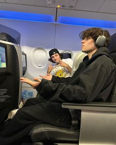 two people sitting on an airplane with headphones in their ears and one person holding his hand out