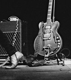 a black and white photo of a person's feet next to an electric guitar