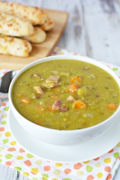 a white bowl filled with green soup next to crackers on a wooden cutting board